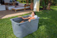 Woman using a grey Frozin cold plunge tub with a headrest beside a patio